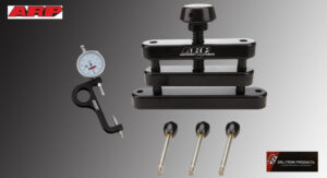 Precision tools including a dial gauge, a clamping device, and four metal pins on a gray background.
