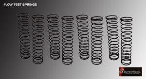 Various sizes of metal coil springs arranged in a row on a gray surface.