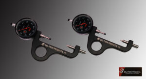 Two black dial indicators with red needles and metal pins on a gray background.