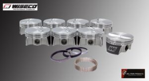 A set of shiny metal pistons with rings and gaskets arranged on a surface.